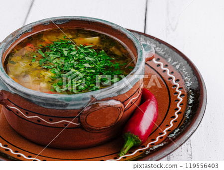 Traditional ukrainian cabbage soup with parsley and red chili pepper on white wooden table background 119556403