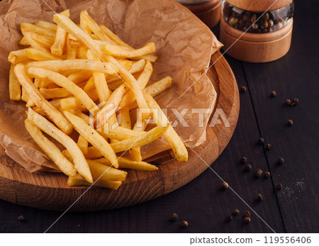 French fries sitting on wooden board with salt and pepper shakers French fries sitting on wooden board with salt and pepper shakers 119556406