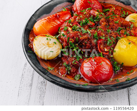 Spicy beef stew garnished with fresh herbs and vegetables on rustic plate 119556420