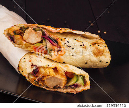 Two delicious chicken shawarma wraps lying on black plate Two delicious chicken shawarma wraps lying on black plate 119556530
