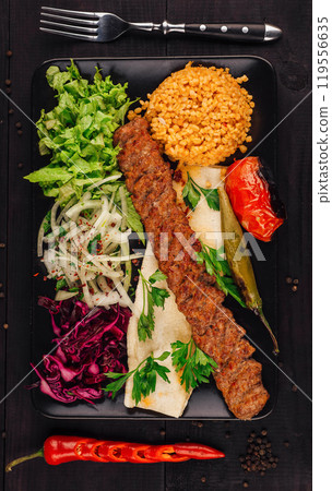 Lulah kebab being served on black plate with fresh vegetables and bulgur 119556635