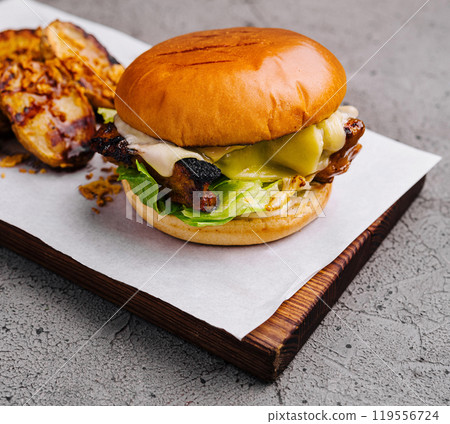 Burger with chicken, cheese and lettuce served on wooden board with fried potato wedges 119556724