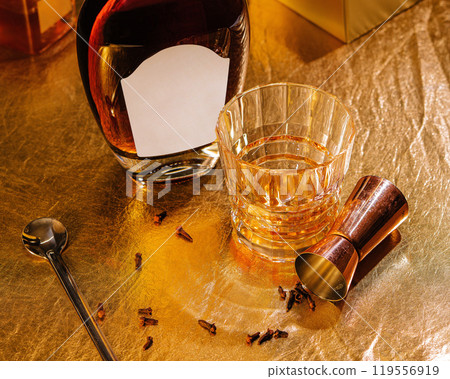 Bottle and glass of whiskey with cocktail making equipment on gold background Bottle and glass of whiskey with cocktail making equipment on gold background 119556919