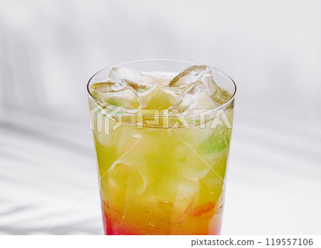 Colorful layered cocktail standing on white cube with tropical shadow 119557106