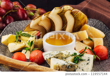 Gourmet cheese plate offering variety of textures and flavors with honey and grapes 119557144