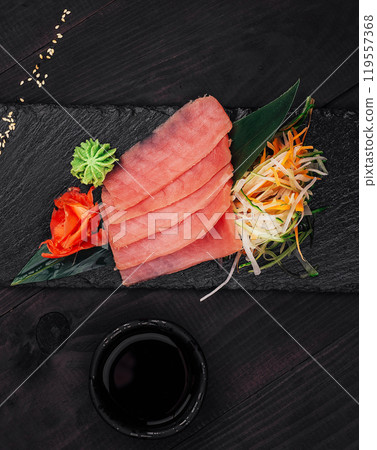 Slices of fresh tuna sashimi with soy sauce and wasabi on black stone plate 119557368