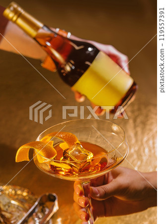 Bartender pouring alcoholic beverage into coupe glass with orange peel Bartender pouring alcoholic beverage into coupe glass with orange peel 119557391