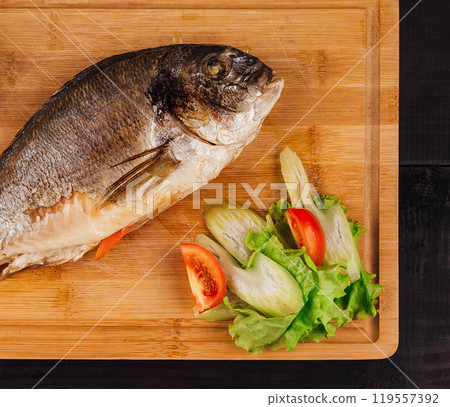 Dorado fish lying on wooden board with lemon and vegetables 119557392