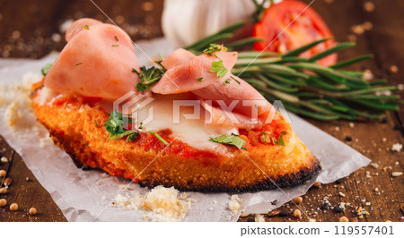 Delicious bruschetta with tomato sauce, ham and cheese lying on paper on a wooden table Delicious bruschetta with tomato sauce, ham and cheese lying on paper on a wooden table 119557401