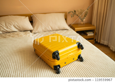 Yellow suitcase on bed indoors entering hotel room, travelling to resort copy space.  119559967
