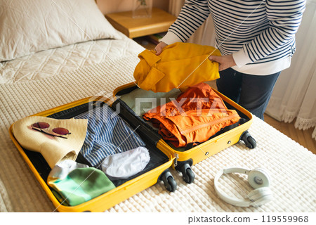 Open yellow suitcase with different family clothes and accessories on sofa. Woman packing suitcase for trip on floor indoors, close up Open yellow suitcase with different family clothes and accessories on sofa. Woman packing suitcase for trip on floor indoors, close up 119559968