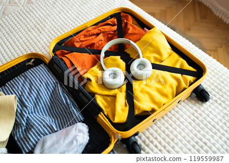 Open yellow suitcase with different family clothes and accessories on bed in light bedroom Open yellow suitcase with different family clothes and accessories on bed in light bedroom 119559987