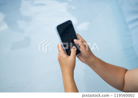 Young woman hand holding a black-screen cell phone outdoors on blue background Young woman hand holding a black-screen cell phone outdoors on blue background 119560002