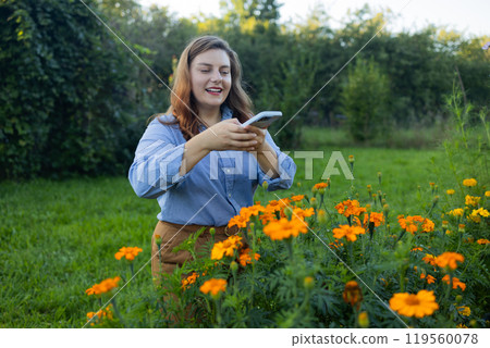 Shot of an happy female Caucasian farmer working in her yard using a smartphone and taking a photo. Gardener using mobile phone. The concept of gardening, growing and caring for flowers and plants. 119560078