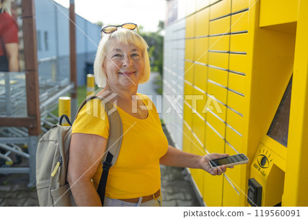 Happy smiling 50s senior woman client with smart phone at outdoor automated parcel machine hoosing operation he touch screened on smart background 119560091