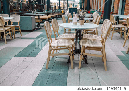 Wooden chairs with a green flowers in the middle of the table of an outdoor restarurant Wooden chairs with a green flowers in the middle of the table of an outdoor restarurant 119560149