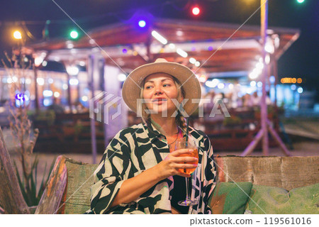 Female tourist on summer vacation drinking cocktail at night at beach bar 119561016
