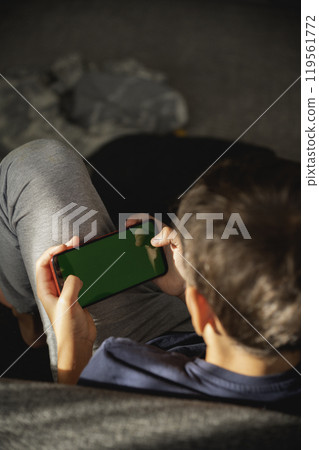 Child looking at phone screen. focus on phone. view from back Child looking at phone screen. focus on phone. view from back 119561772