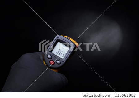 A gloved hand holds an industrial thermometer on a black background. 119561992