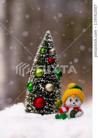 Miniature figurines of Christmas tree and a snowman in the snowy forest. 119562087