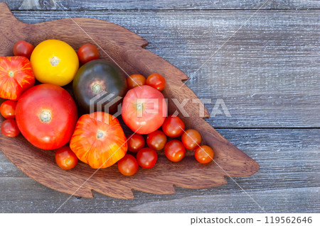 Variety of colorful tomatoes on the wooden plate on the garden table. 119562646
