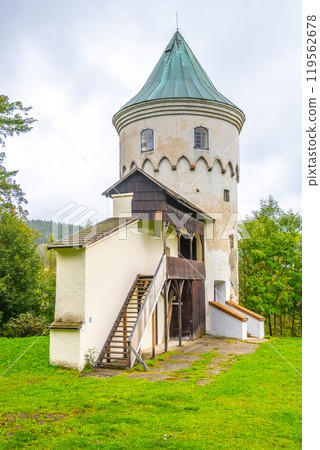 Slikovka Tower, part of the historic Slik Castle, stands amidst lush greenery in Jachymov, Ore Mountains. The structure features a distinctive conical roof and rustic wooden elements. 119562678