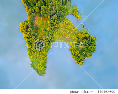 A lush green peninsula juts out into tranquil blue waters. Dense vegetation covers the land, creating a vibrant contrast A lush green peninsula juts out into tranquil blue waters. Dense vegetation covers the land, creating a vibrant contrast 119562690