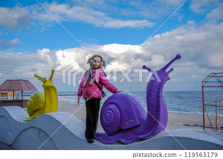 Girl and snails against the backdrop of a seascape. On the Odessa embankment there are decorative snails and a girl against the backdrop of a cloudy sky. 119563179