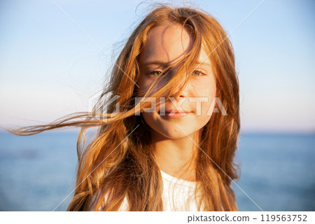Portrait of beautiful teenage girl with long flowing red hair against the background of the sea in summer at sunset 119563752