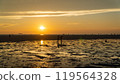 Group walking on beach during sunset, admiring red sky at dusk over water 119564328