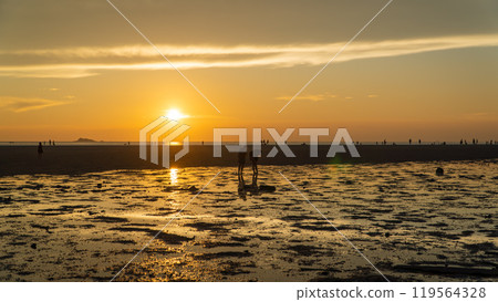 Group walking on beach during sunset, admiring red sky at dusk over water Group walking on beach during sunset, admiring red sky at dusk over water 119564328
