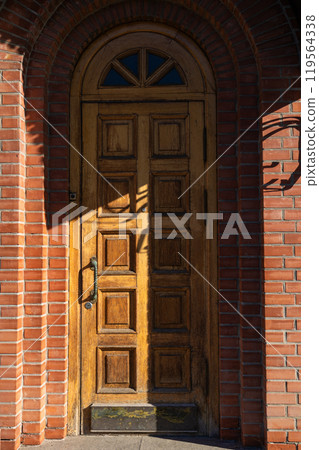 A tall, narrow, old, wooden door. Entrance to the brick building A tall, narrow, old, wooden door. Entrance to the brick building 119564338