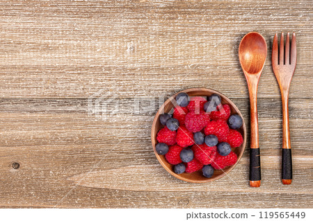 Mix of blueberries and raspberries in a plate with wooden fork and spoon. Mix of blueberries and raspberries in a plate with wooden fork and spoon. 119565449