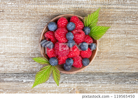 Plate with raspberries and blueberries with leaves on the wooden rustic table. 119565450