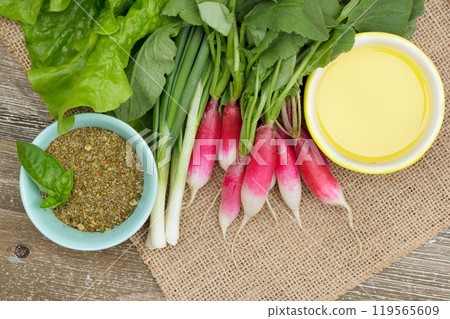Fresh ripe vegetables on the wooden table with burlap table cloth - radish, green onion, lettuce, dried herbs in a little prep bowl with basil leaves and olive oil are ready to cook salad. Fresh ripe vegetables on the wooden table with burlap table cloth - radish, green onion, lettuce, dried herbs in a little prep bowl with basil leaves and olive oil are ready to cook salad. 119565609