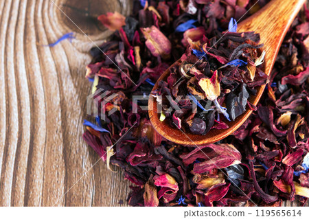 Tea mix of karkade, flowers and berries in a spoon and on the table. Tea mix of karkade, flowers and berries in a spoon and on the table. 119565614