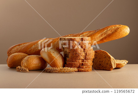 Sliced bread, baguette, and French buns with wheat ears on a beige background. Sliced bread, baguette, and French buns with wheat ears on a beige background. 119565672