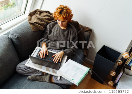 young red-haired woman sitting on soft sofa in warm sweater, using tablet, working, studying, e-learning young red-haired woman sitting on soft sofa in warm sweater, using tablet, working, studying, e-learning 119565722
