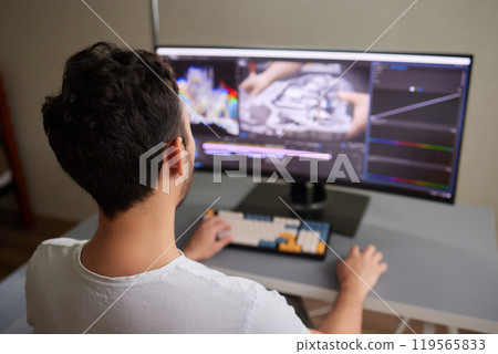back view of young man in the dark studio color grading video with laptop and external monitor back view of young man in the dark studio color grading video with laptop and external monitor 119565833
