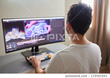 back view of young man in the dark studio color grading video with laptop and external monitor back view of young man in the dark studio color grading video with laptop and external monitor 119565841