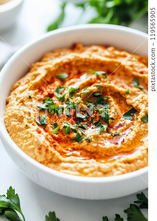 A bowl of creamy roasted red pepper hummus garnished with herbs, ready for tasting 119565905