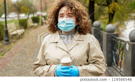 Pandemic walk. Outdoor quarantine. Sad depressed overweight woman with curly hair in medical mask strolling on empty autumn street. 119566546