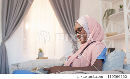 Healthcare learning. Medical education. Nurse course. Cheerful woman intern student reading research book studying disease on sofa at clinic. Healthcare learning. Medical education. Nurse course. Cheerful woman intern student reading research book studying disease on sofa at clinic. 119566560