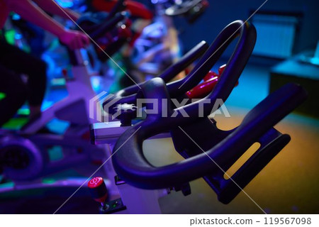 Row of exercise bikes in gym under electric blue lighting Row of exercise bikes in gym under electric blue lighting 119567098