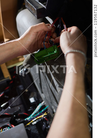 Auto electrician is connecting a wiring to car amplifier close up. 119567132