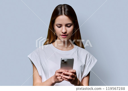 Young beautiful woman using smartphone on grey studio background 119567288