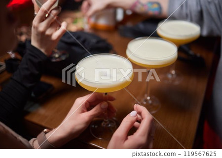 A woman holds a cocktail in her hand, with her fingers wrapped around the glass 119567625