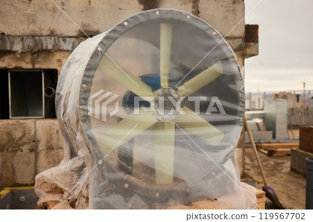 A huge fan covered in plastic sits on a rooftop against the skyline A huge fan covered in plastic sits on a rooftop against the skyline 119567702