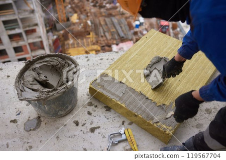 A construction worker is applying mortar on insulation board at a building site 119567704