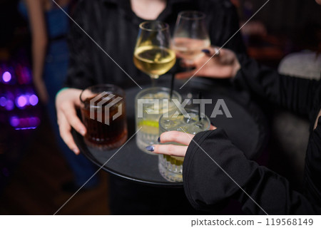 A woman holds a cocktail in her hand, with her fingers wrapped around the glass A woman holds a cocktail in her hand, with her fingers wrapped around the glass 119568149